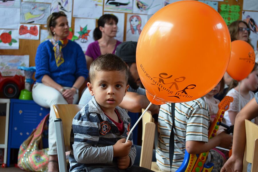 Ein kleiner Junge auf einer Veranstaltung der Bürgerstiftung Berlin hält einen orangefarbenen Luftballon in der Hand